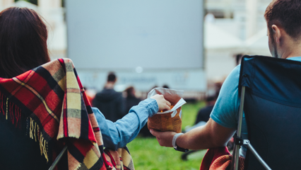 A couple sitting in a park sharing a snack while waiting for a movie to start