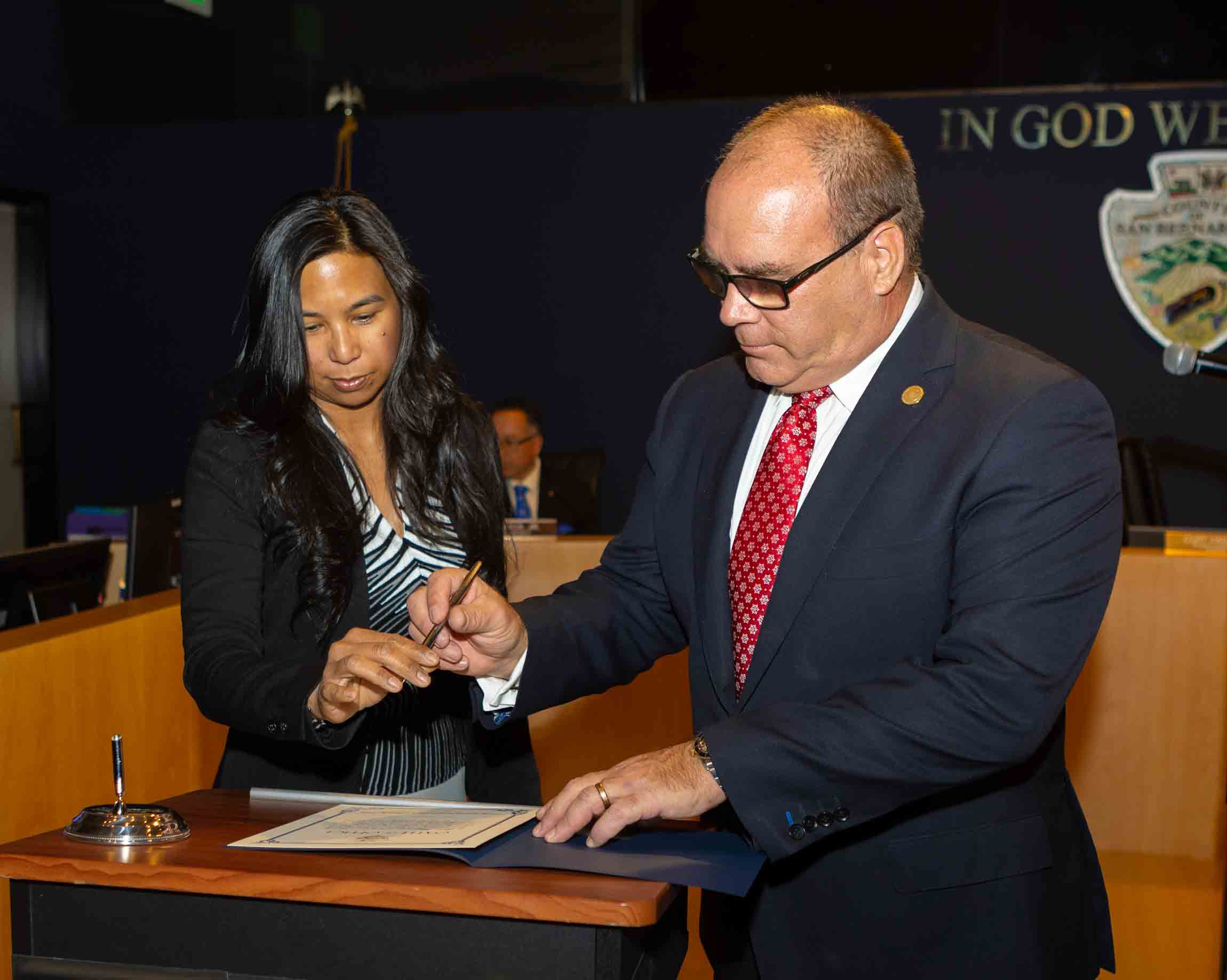 Rossana Hagman handing Supervisor Hagman a pen to sign his oath of office certificate.