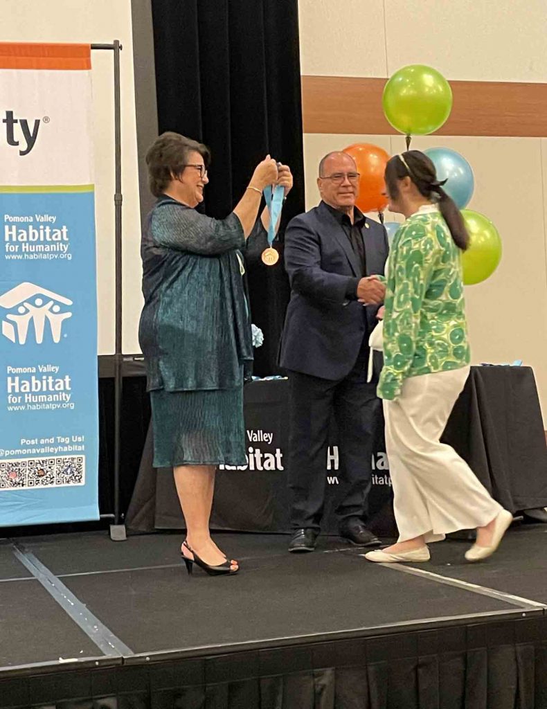 Supervisor Hagman shaking hands with an award recipient on stage.