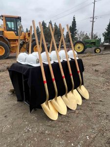 Five shovels resting on table with hard hats for groundbreaking ceremony