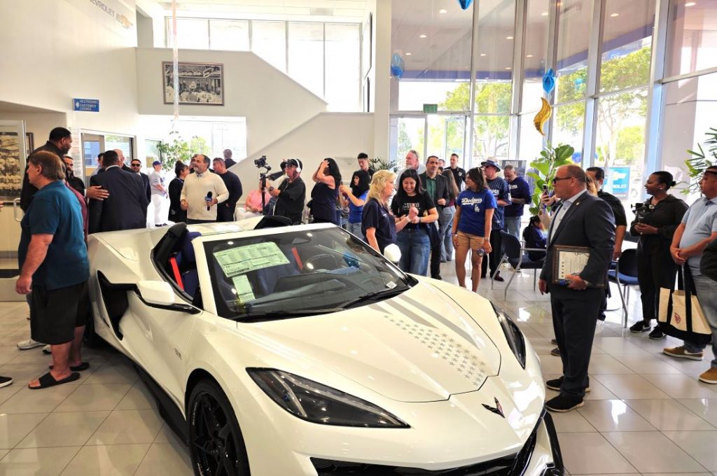 Guests gather around a white Corvette inside Orel Hershiser Chevrolet during the grand opening celebration.