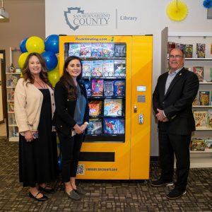 Three people pose beside new book vending machine at San Bernardino County Library.