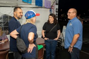 Four people chat under a tent at a community event in the evening.