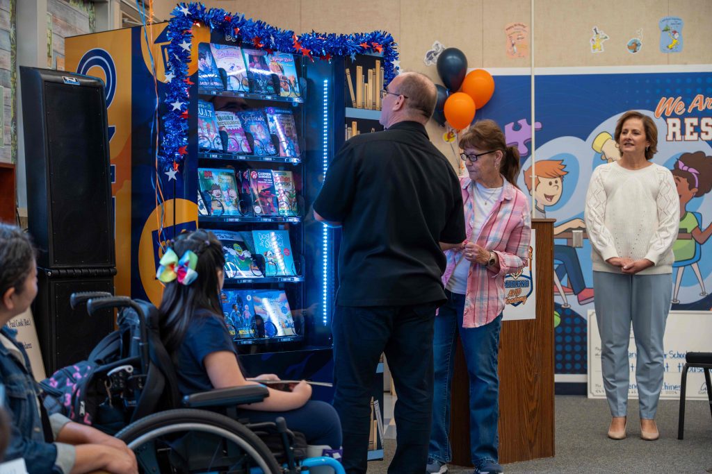 Supervisor Curt Hagman demonstrates the new book vending machine with students and school staff watching.