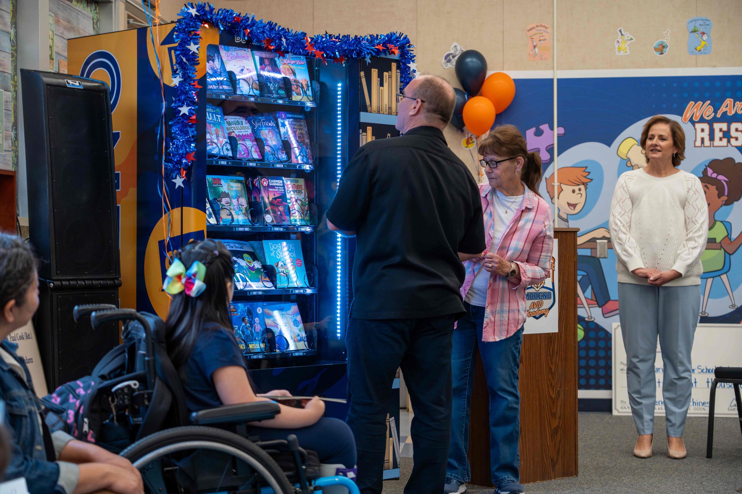 Supervisor Curt Hagman demonstrates the new book vending machine with students and school staff watching.
