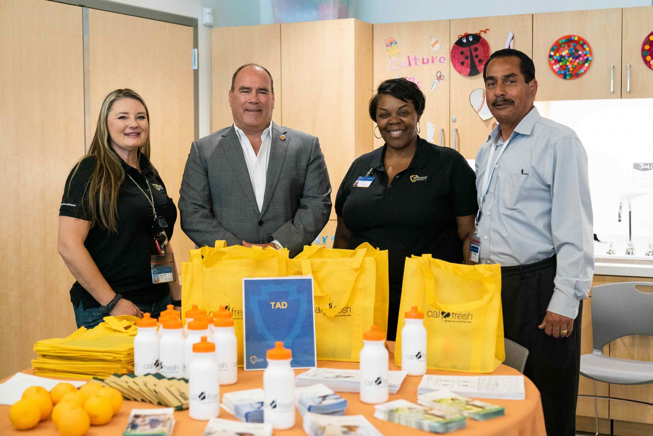 Supervisor Curt Hagman poses with two females and a male behind a table of CalFresh giveaways at the 2022 West End Job Fair.