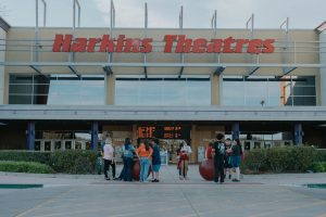 A group of people gathers outside the Harkins Theatres entrance near the ticket counters.