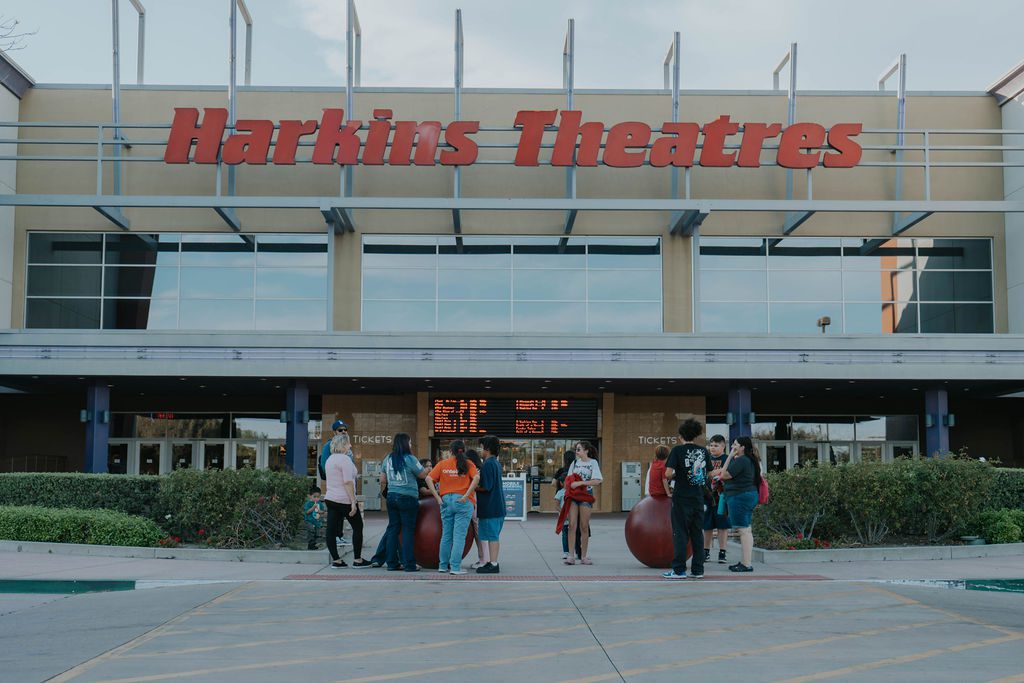 A group of people gathers outside the Harkins Theatres entrance near the ticket counters.