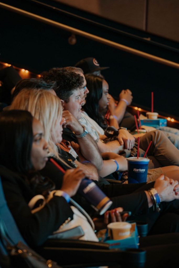Audience members seated at Harkins Theatres watching a film, holding drinks and popcorn.