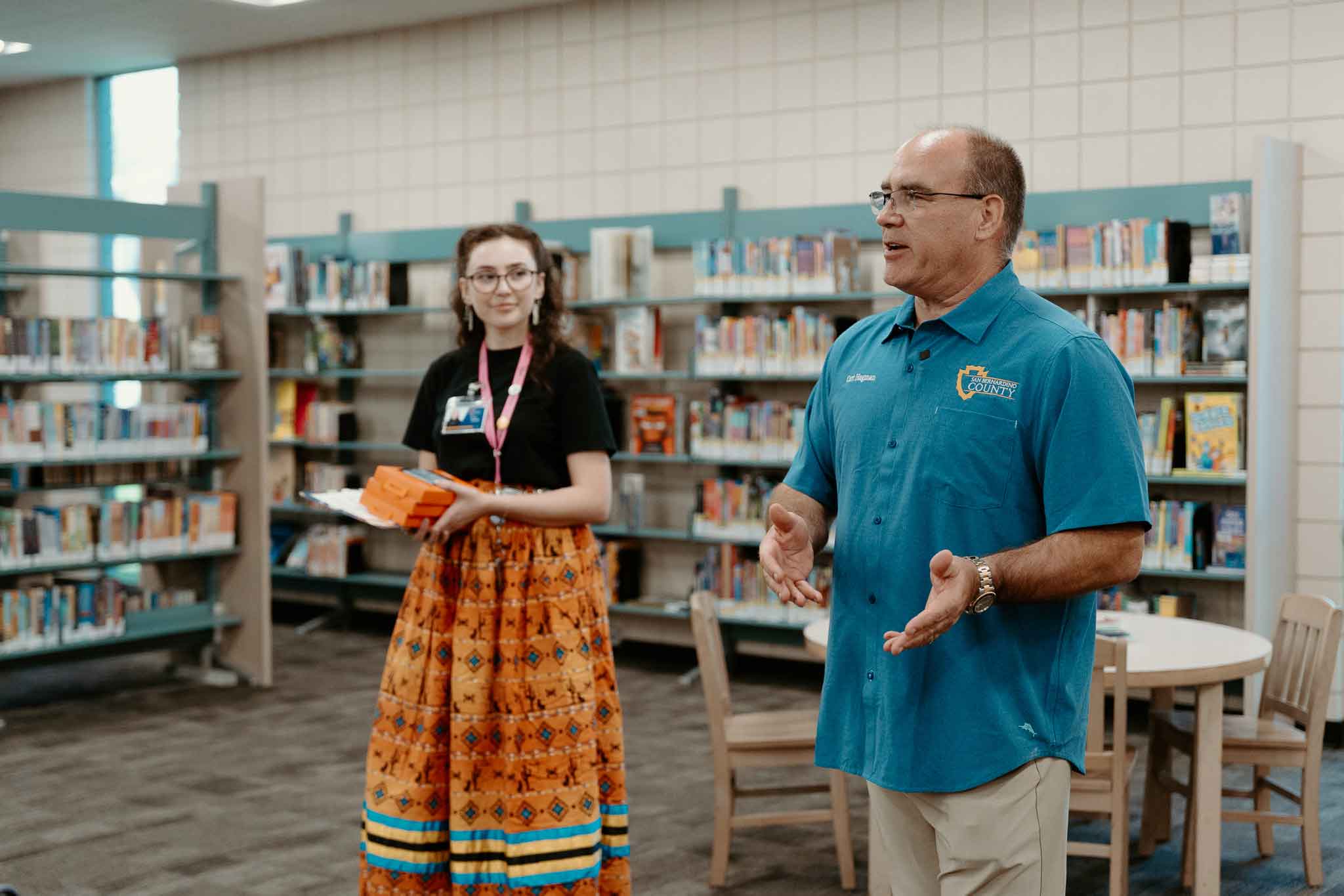 Supervisor Curt Hagman speaks at a library as a staff member holds tablets to his right.