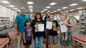 Supervisor Curt Hagman poses with families holding reading certificates and tablets.