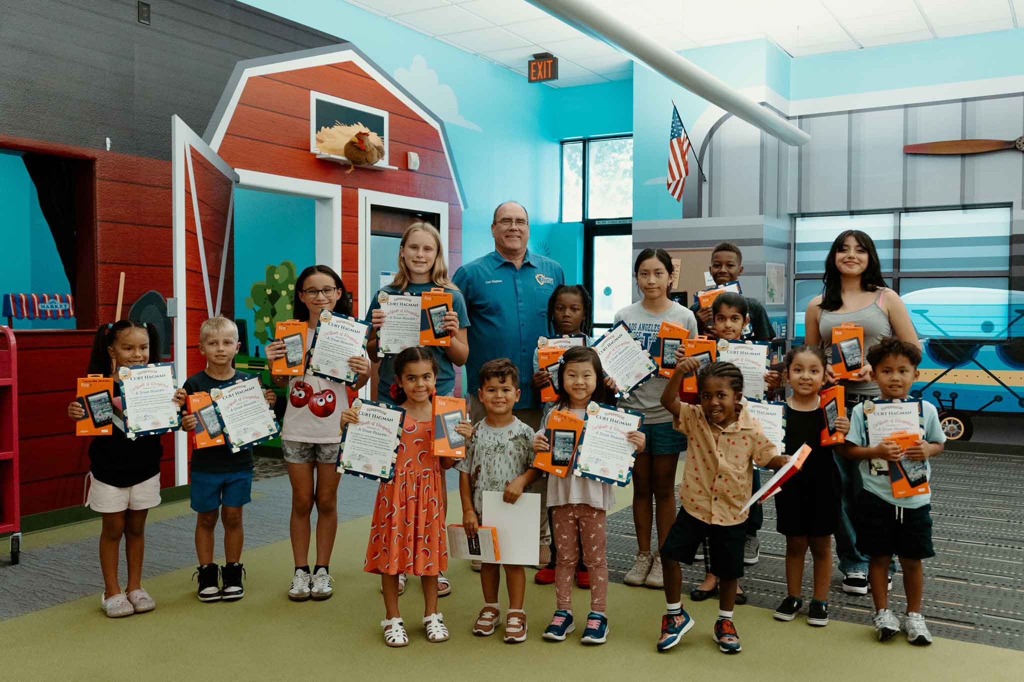 Supervisor Curt Hagman with students holding reading certificates and tablets in a kid's room in the library.