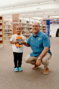 Supervisor Curt Hagman posing with a child holding an Amazon Fire tablet in a library.