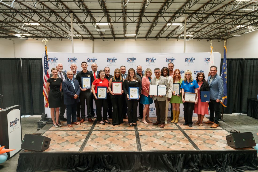 Community leaders and partners gather on stage, holding certificates at the West End Regional Navigation Center groundbreaking.