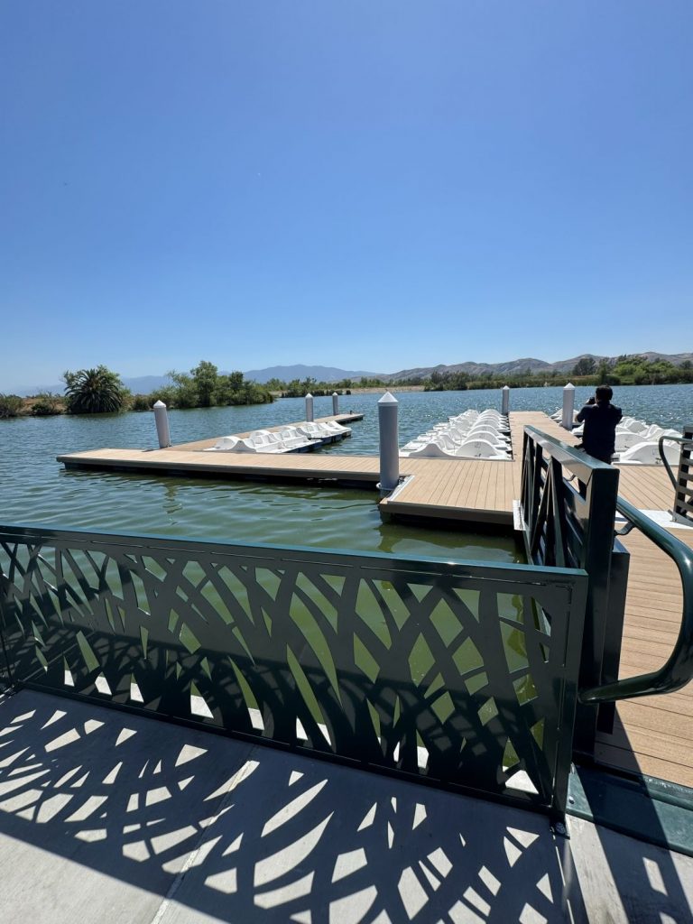 Wooden dock with rows of white paddle boats on the lake at Prado Regional Park under a clear blue sky.