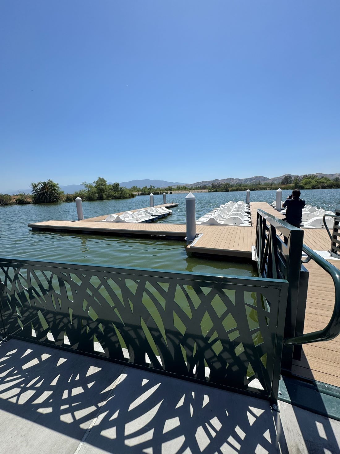Wooden dock with rows of white paddle boats on the lake at Prado Regional Park under a clear blue sky.