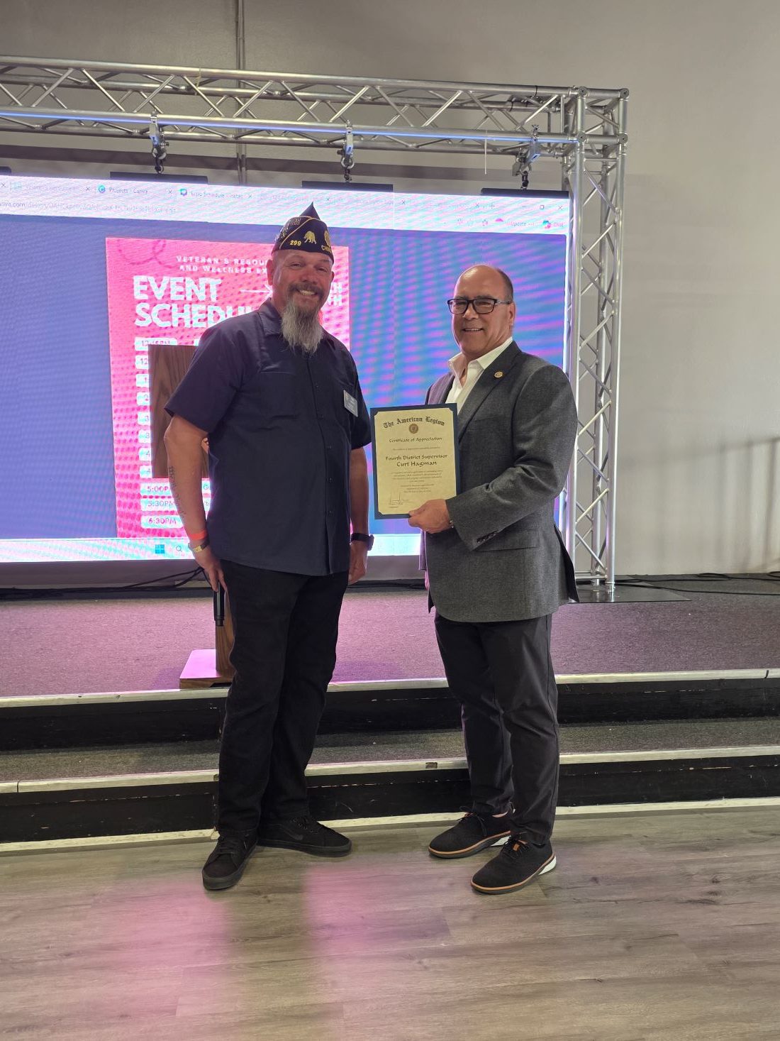 A male presents Supervisor Hagman with a certificate thanking him for his contribution to the American Legion.