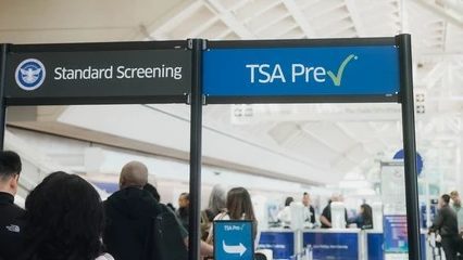Passengers line up beneath Standard Screening and TSA PreCheck signs at an airport security checkpoint.