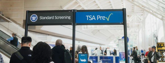 Passengers line up beneath Standard Screening and TSA PreCheck signs at an airport security checkpoint.