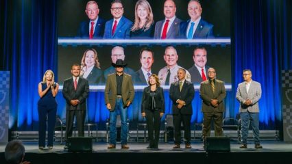 San Bernardino County Leadership stand on stage at an event, with a large screen behind them displaying portraits of community and government leaders.