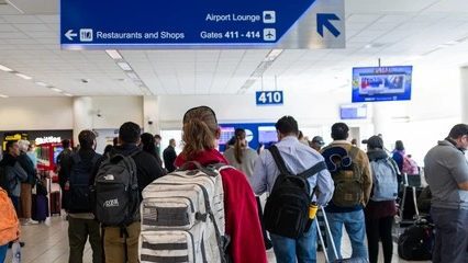 Travelers wait near Gate 410 beneath airport signs directing passengers to gates, restaurants, shops, and the lounge.